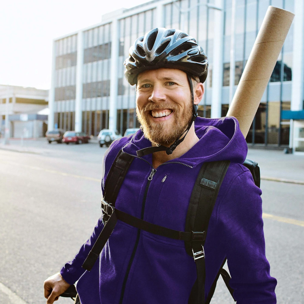 linexo Fahrrad Versicherng Junger Mensch in lila Hoodie mit Fahrradhelm lehnt am Fahrrad vor Bürogebäuden