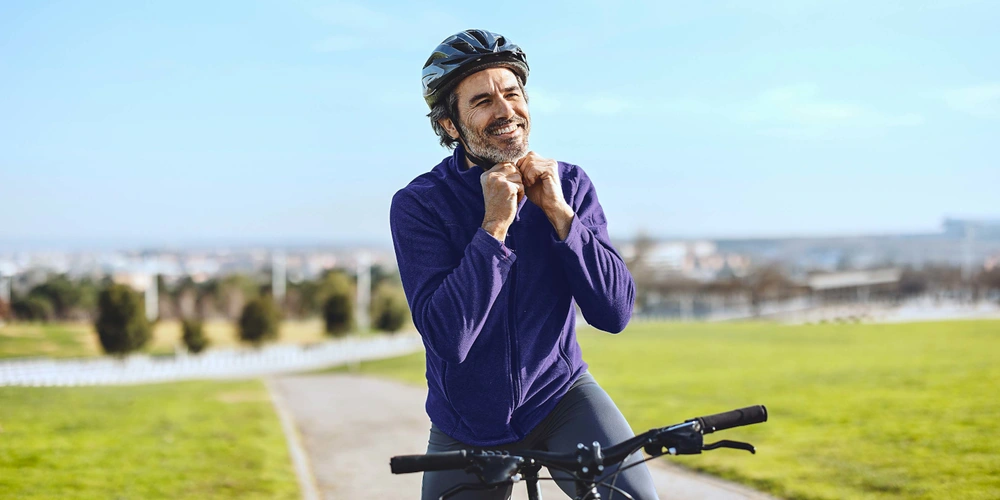 Lachender Fahrradfahrer Lachender Radfahrer mit Helm auf einer Wiese, im Hintergrund eine Stadtlandschaft.